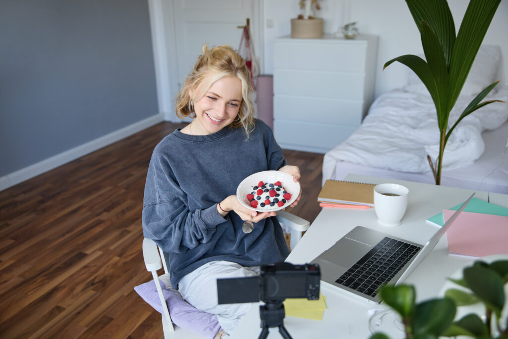 Portrait of young woman talking to audience, recording vlog on digital camera, showing her breakfast, talking about healthy food and lifestyle